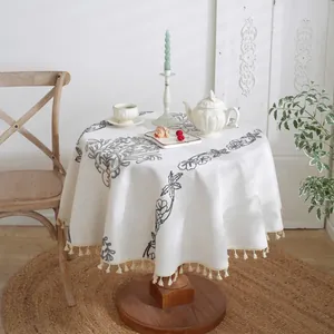 Detalle de mantel redondo de jacquard con motivos florales grises y borlas de flecos