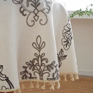Detalle de mantel de estilo nórdico con bordado floral gris y borlas de flecos beige