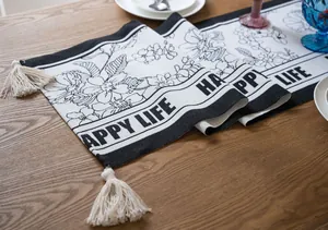 Detalle del camino de mesa jacquard nórdico con patrón floral en blanco y negro y borlas