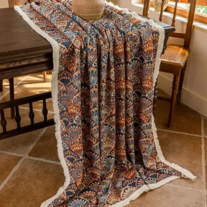 Detail of bohemian jacquard tablecloth with warm orange patterns and cream fringe tassels