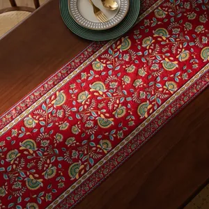 Detail van rode vintage tafelloper met bloemmotieven op een donkere houten tafel
