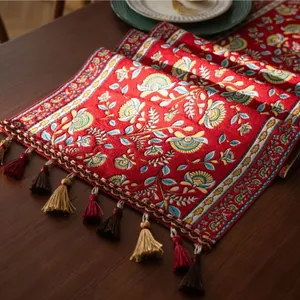 Detailopname van rode jacquard tafelloper met bloemmotieven en kleurrijke kwastjes