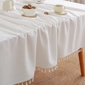 Minimalist white cotton tablecloth with fringe on a wooden table for home decor