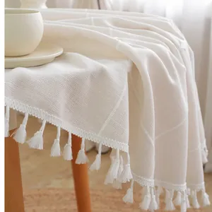 Close-up of beige linen tablecloth featuring elegant white tassels on a wooden table
