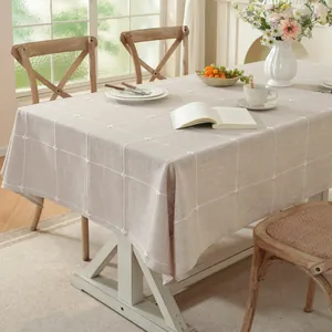 Detalle de mantel bordado a cuadros beige con borlas sobre mesa de madera rústica