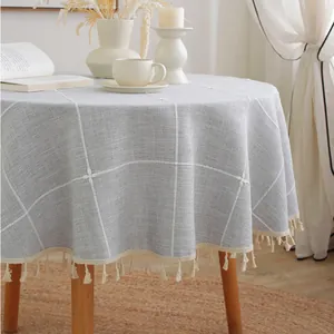 Detail of grey checkered round tablecloth with tassel fringe on a wooden dining table