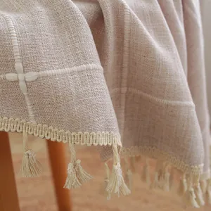 Detail of beige round tablecloth with grid embroidery and fringe tassels in Nordic style