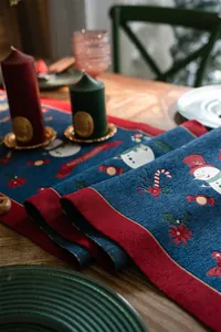 Detail of Christmas table runner with snowman jacquard and festive tassels on wooden table