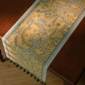 Gele tafelloper met paisley-patroon, blauwe rand en kwastjes op houten tafel