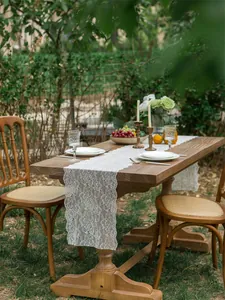 Detailed close-up of white floral lace table runner on a rustic wooden table setup