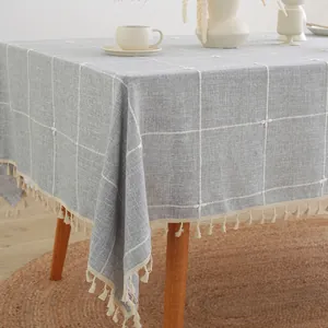 Detail van lichtgrijs linnen-look tafelkleed met wit borduurraster en beige kwastjes