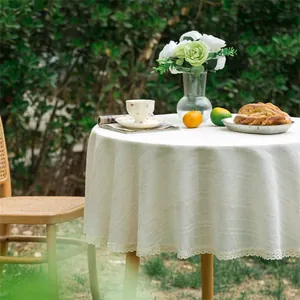Detail van rond beige linnen tafelkleed met kantafwerking op een ronde tuintafel buiten