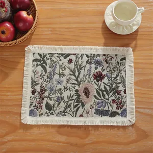 Detail of woven floral placemat with tassels and botanical patterns on a wooden table