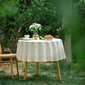 Detail van rond beige linnen tafelkleed met delicate gele kantafwerking buiten in de tuin