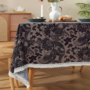 Detail der dunkel geblümten Tischdecke mit edler weißer Spitzenkante auf Holztisch