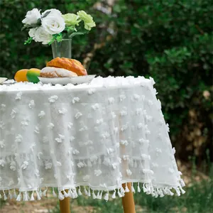 Detail of white round tablecloth with 3D floral appliques and delicate fringe edge