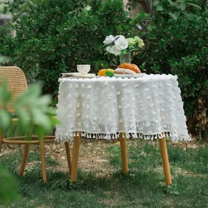 Close-up of white round tablecloth with 3D tufted flowers and delicate fringe tassels