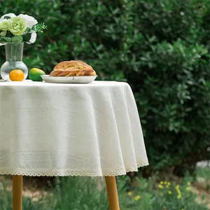 Detail van beige linnen rond tafelkleed met elegante kanten randen op houten tuintafel