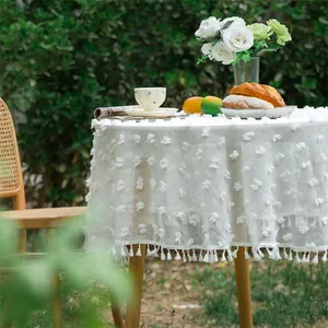 Detailed macro view of white round tablecloth featuring 3D floral textures and fringe edges