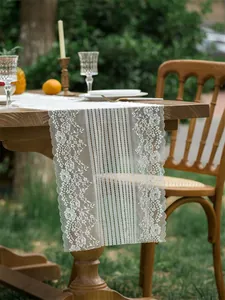 Dettaglio del runner da tavola in pizzo bianco su tavolo in legno per matrimoni all'aperto