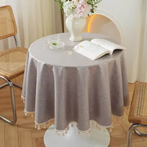 Detail einer runden beige Tischdecke mit Leinentextur und cremefarbenen Fransen am Rand