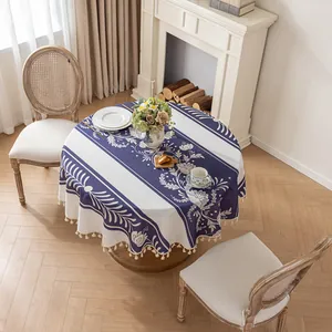 Nappe ronde en coton et lin à fleurs bleues avec pompons blancs sur table en bois