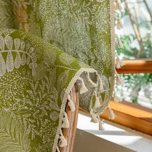Detailed texture of linen fabric with tropical leaf patterns and off-white tassel fringe