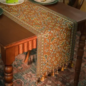 Runner da tavola vintage bohémien con motivi floreali marroni e nappe su tavolo in legno