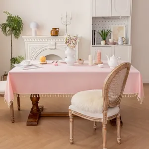 Detailed close-up of light pink linen tablecloth with elegant white fringe on a wooden table