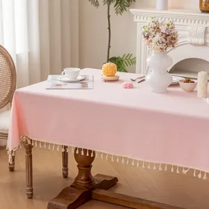 Pale pink rectangular fabric tablecloth with elegant cream fringe trim in a cozy home setting