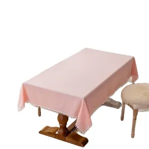 Pink cotton square tablecloth with white pom-pom fringe on a wooden table in home setting