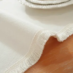 Vue détaillée du chemin de table en coton beige avec pompons et texture en lin naturel