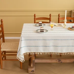 Detail van crème tafelkleed met marineblauwe geborduurde bladeren en franje aan de rand