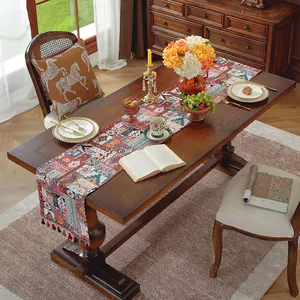 Dettaglio runner da tavola bohémien con motivi colorati e nappe rosse su tavolo in legno