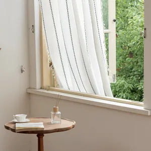 Detail of white striped curtain with blue embroidery and white pom-pom tassel trim