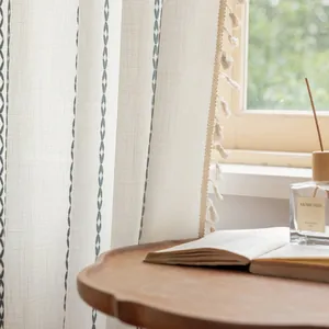 Detail of cream striped curtain with blue woven patterns and bohemian fringe trim