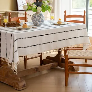 Detail van een crèmekleurig tafelkleed met zwarte geometrische lijnen en franjes