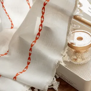 Macro shot of white linen curtain featuring orange geometric embroidery and tassel details
