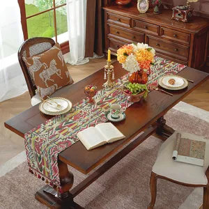 Dettaglio runner da tavolo boho con motivi geometrici e nappe rosse su legno massiccio