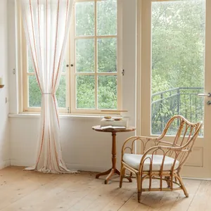 Detail of white striped curtains with orange chain embroidery near a rattan chair