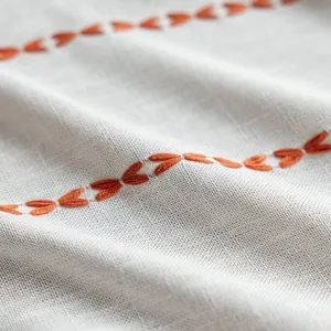 Detailed macro view of orange embroidered leaf patterns on beige striped fabric curtain