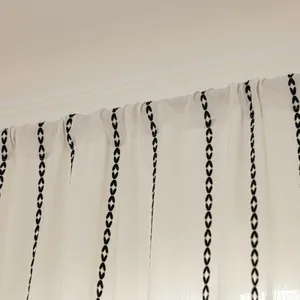 Close-up of cream striped fabric with black geometric embroidery and textured weave