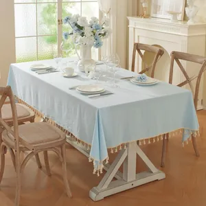 Detail of light blue rectangle tablecloth with cream cotton tassels on wooden table
