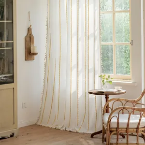 Detail of ivory polyester striped curtain with yellow tassels in a cozy home setting