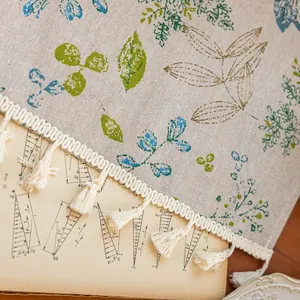 Close-up of linen fabric with blue botanical leaf prints and white tassel edges