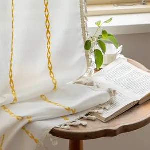 Close-up of white striped polyester curtain with yellow embroidery and tassel fringe