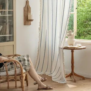 Close-up of beige polyester striped curtain with blue embroidery and tassel trim details