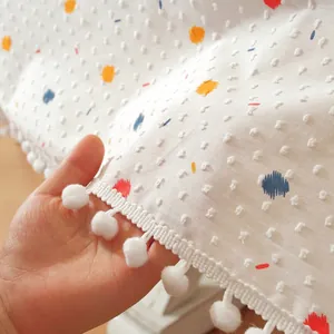 Détail de nappe en coton blanc avec pois colorés et bordure décorative à pompons blancs
