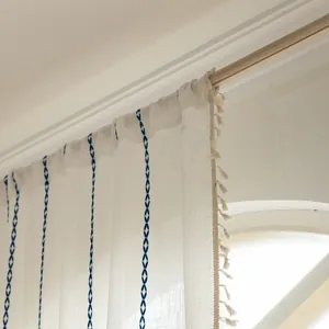 Detail of white striped curtain with blue diamond embroidery and beige tassel edges