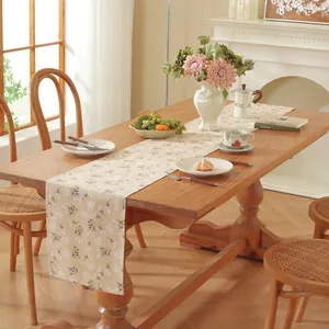 Détail d'un chemin de table crème avec broderie florale sur une table en bois naturel